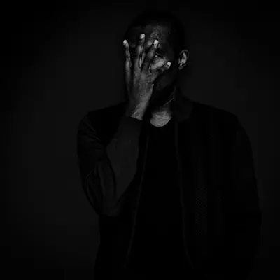 Portrait studio low key en noir et blanc d'un homme masquant son visage avec sa main.