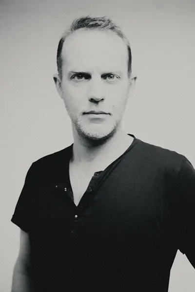 Portrait studio en noir et blanc d'un homme en t-shirt noir au regard direct.