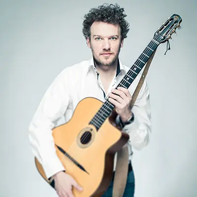 Portrait studio en couleur d'un guitariste tenant une guitare acoustique en chemise blanche.