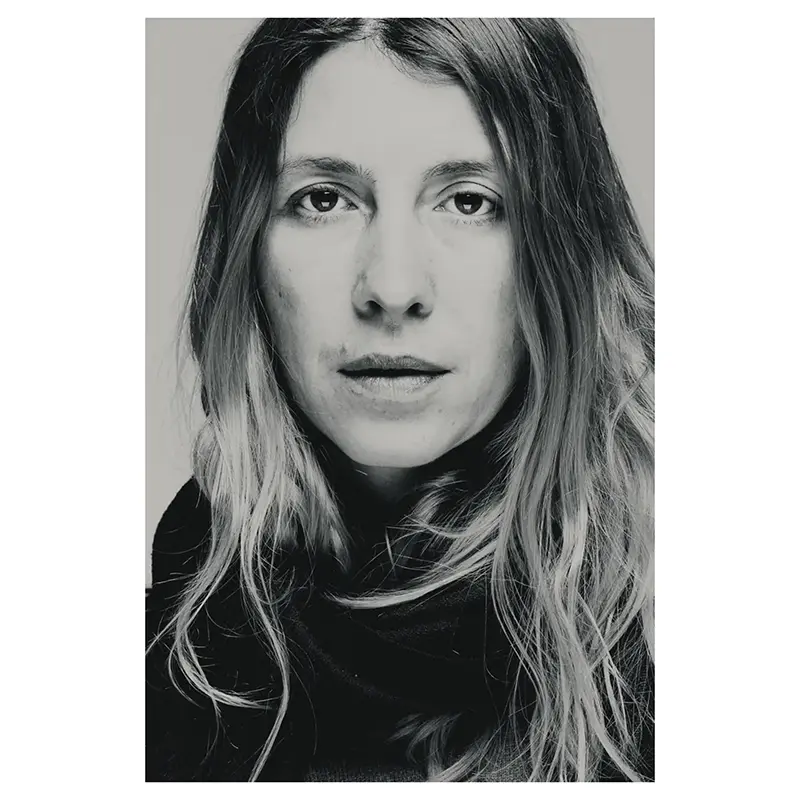 Portrait noir et blanc d’une femme aux cheveux ondulés, cadrage serré, regard caméra, lumière douce, écharpe sombre, en studio photo, style éditorial.