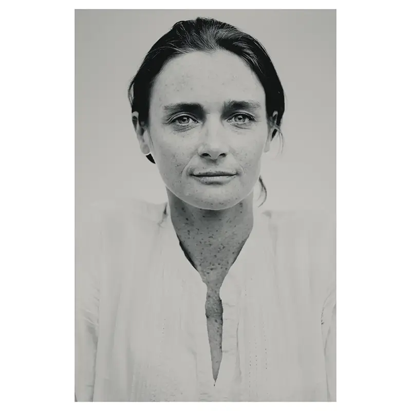 Portrait professionnel
noir et blanc d’une femme aux taches de rousseur, cheveux relevés, plan poitrine, regard caméra, lumière douce, chemise blanche, fond studio neutre — photographe de portrait à Dieulefit.