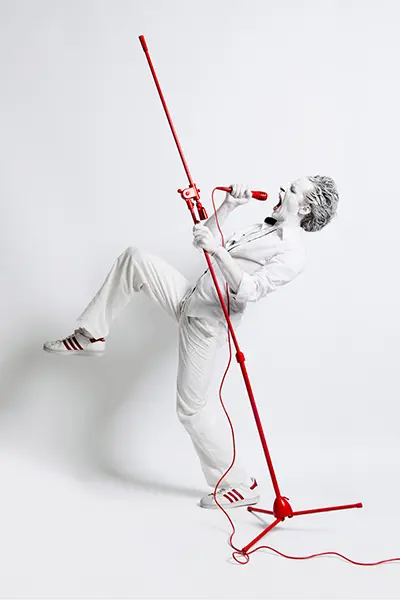 Portrait studio en pied d'un homme habillé en blanc tenant un pied de micro rouge vif dans une pose dynamique sur fond blanc.