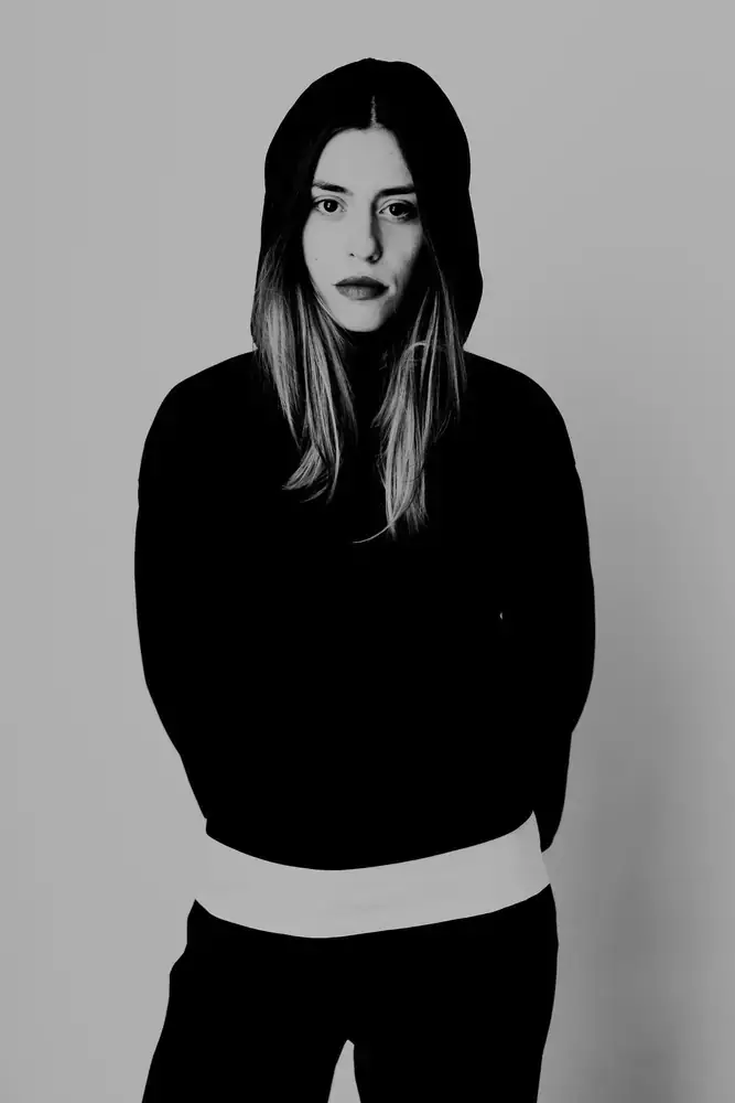 Portrait en pied d’une femme avec sweat à capuche et chemise, studio, noir et blanc.