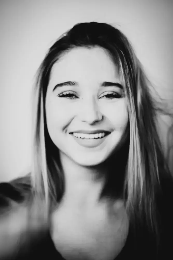 Portrait rapproché d’une jeune femme souriante, noir et blanc, fond neutre.